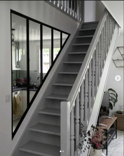 Verrière triangulaire sur-mesure sous un escalier, profilés noirs, vue depuis le rez-de-chaussée.