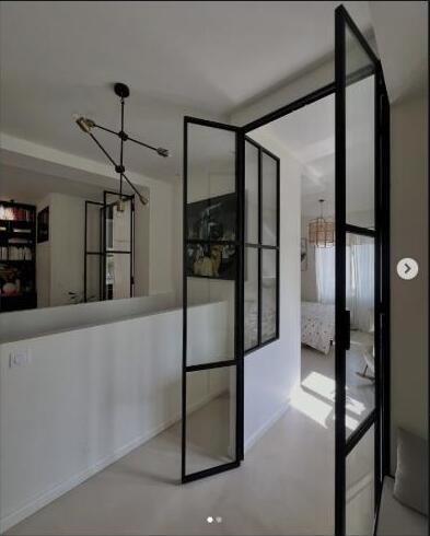 Vue d'ensemble d'un couloir avec une porte-verrière ouverte, chambre et cuisine visibles en enfilade.