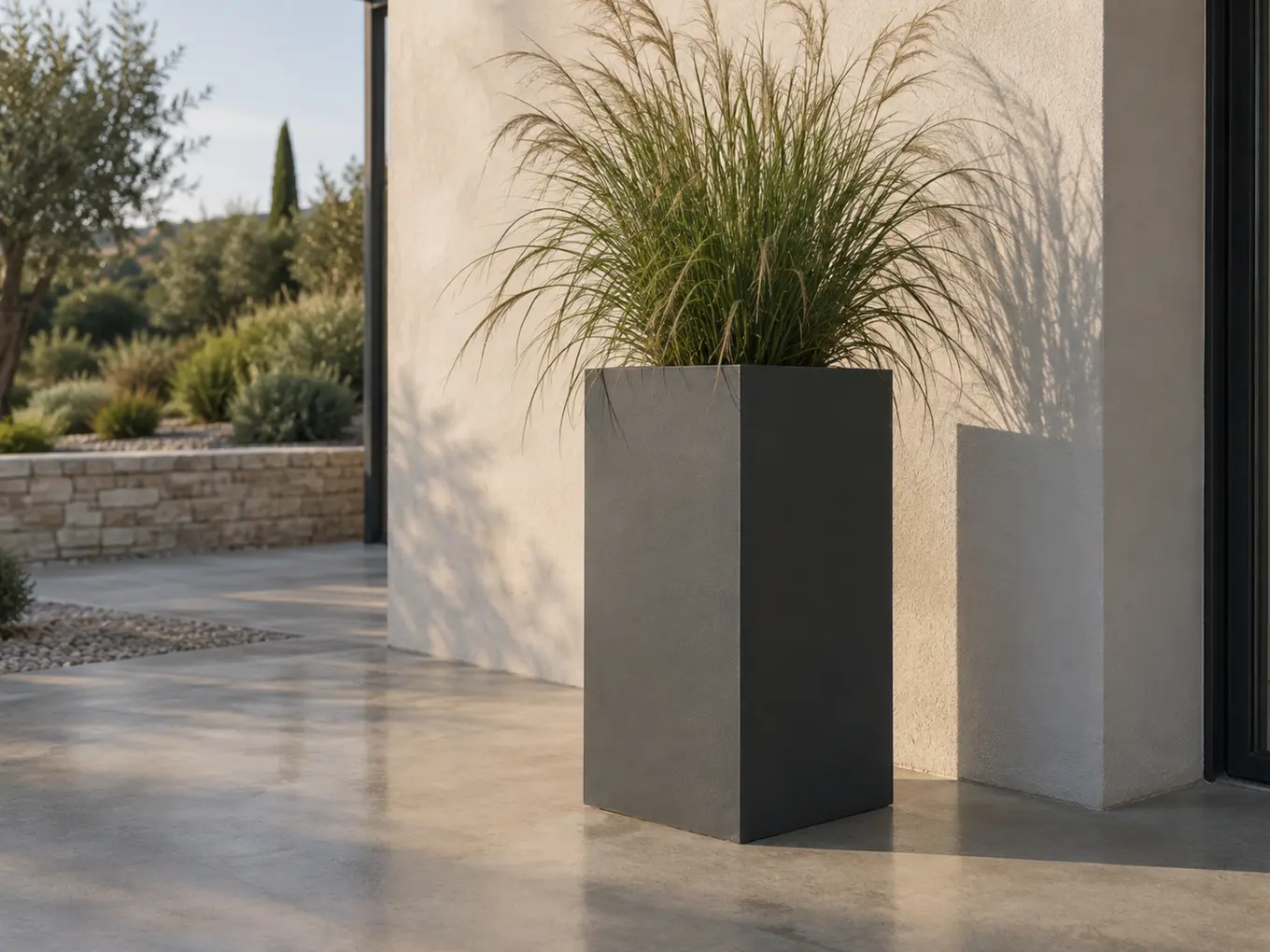 Vue d'artiste d'une colonne-jardinière en acier thermolaqué gris anthracite plantée d'une graminée haute, dans une entrée en béton ciré