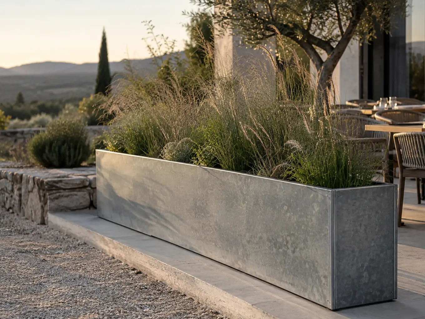 Vue d'artiste d'une jardinière longue en acier galvanisé brut plantée de graminées hautes, en bordure d'une terrasse