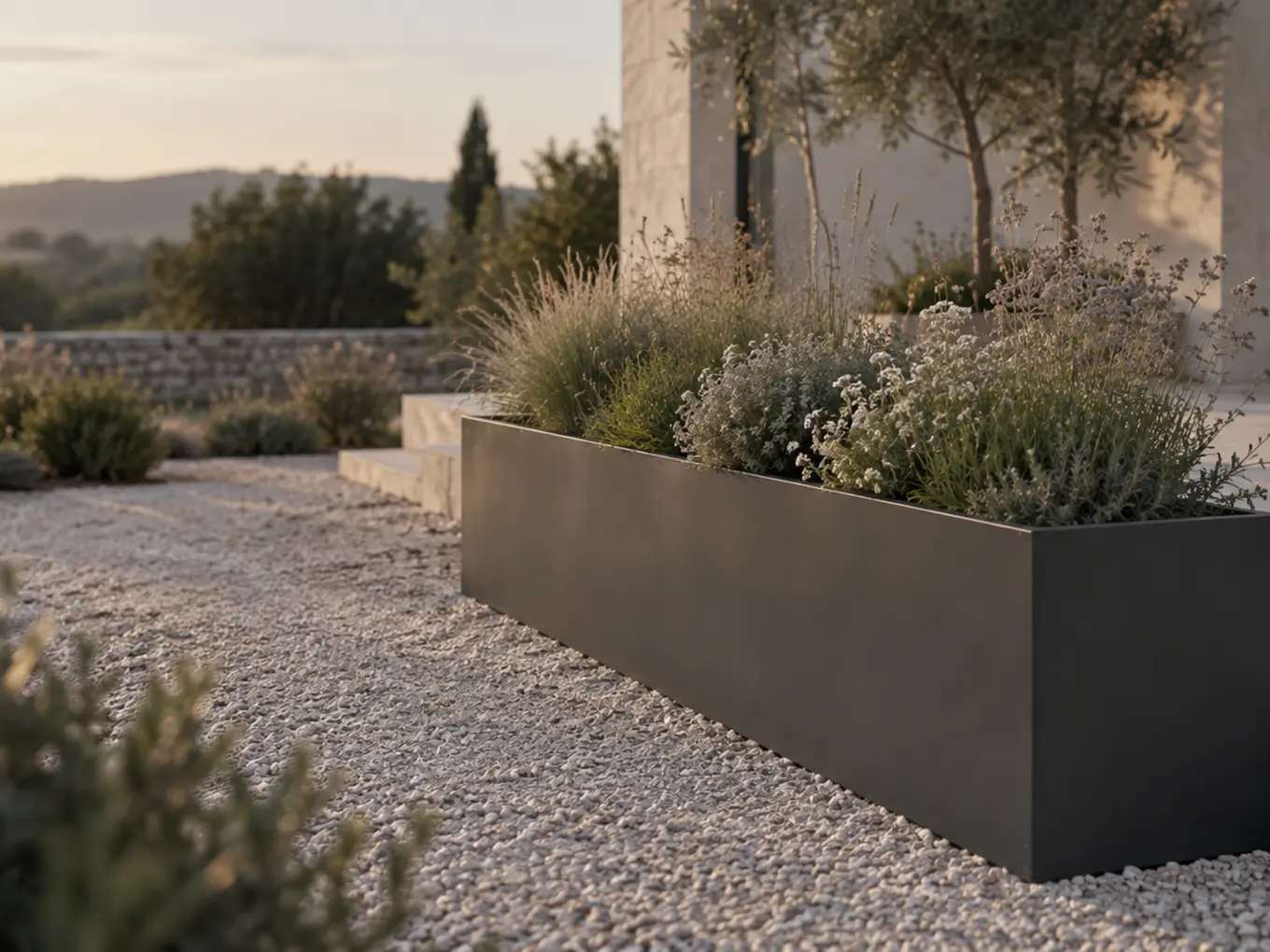 Vue d'artiste d'une jardinière longue en acier thermolaqué gris anthracite plantée de graminées et de vivaces, le long d'une allée de gravier